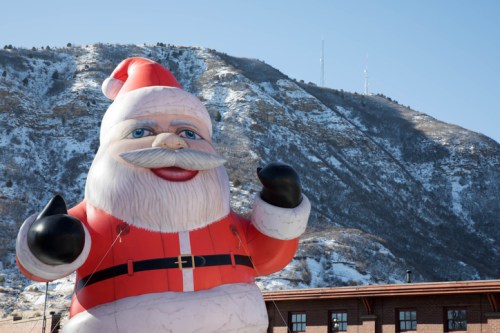 A large inflatable Santa Claus stands in front of a snowy mountain backdrop on a clear day.