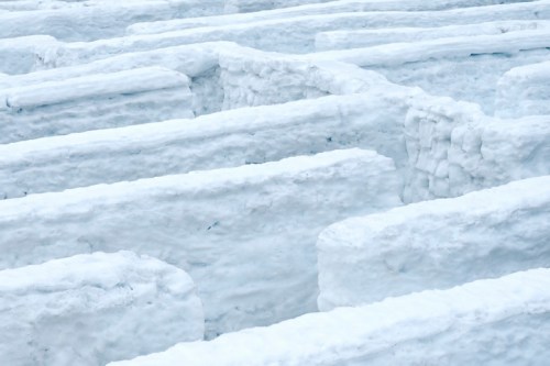 A close-up of a snow maze with high, white walls creating a winding path through the snowy landscape.
