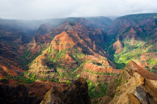 A breathtaking view of colorful, rugged mountains with lush greenery and misty clouds in the background.
