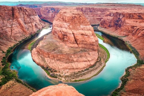 Aerial view of Horseshoe Bend, showcasing a winding river surrounded by red rock formations and lush greenery.