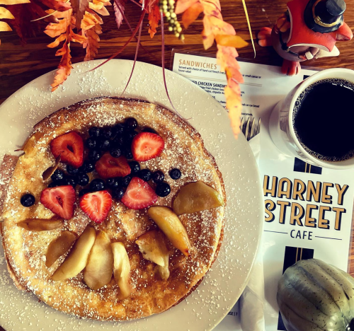 A plate of fluffy pancake topped with strawberries, blueberries, and apple slices, alongside a cup of coffee and a menu.