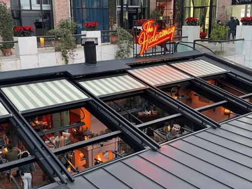 View of a rooftop with striped awnings, overlooking a lively restaurant called "The Hideaway" below.