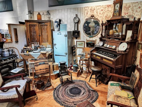 A cozy vintage room filled with antique furniture, a piano, and various collectibles, creating a nostalgic atmosphere.