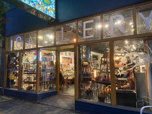 A brightly lit art gallery with large windows displaying various artworks and decorative items.