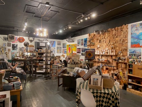 A cozy art shop filled with colorful artwork, wooden decor, and various craft items displayed on shelves and tables.