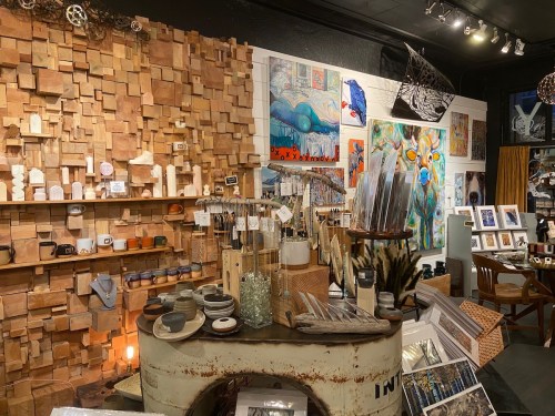A cozy art shop featuring wooden wall decor, various artworks, handmade crafts, and unique home goods displayed creatively.