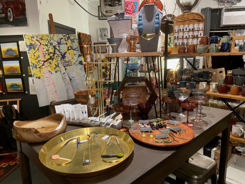 A display of handmade crafts, jewelry, and art in a cozy shop, featuring colorful pottery and decorative items.