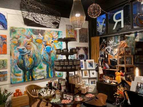 A cozy art shop featuring colorful paintings, decorative items, and a display of candles and crafts on a wooden table.