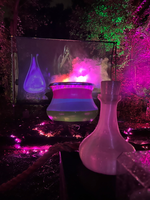 A glowing cauldron surrounded by colorful lights and mist, with a backdrop of a mystical scene.