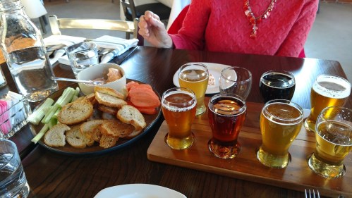 A table setting with a platter of bread and vegetables, alongside a flight of various craft beers.