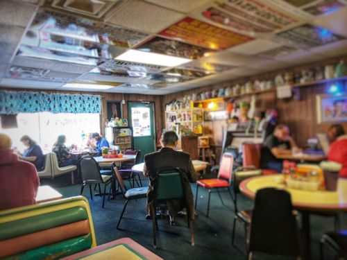 A cozy diner interior with colorful decor, featuring patrons seated at tables and a bright window in the background.