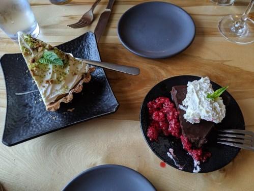 A slice of key lime pie on a black plate and a chocolate dessert with raspberries and whipped cream on another plate.