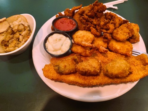A plate of fried fish and shrimp with dipping sauces, accompanied by a side of seasoned potatoes.