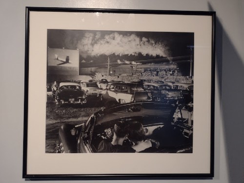 A vintage black-and-white photo of a drive-in theater, with cars parked and a movie screen in the background.