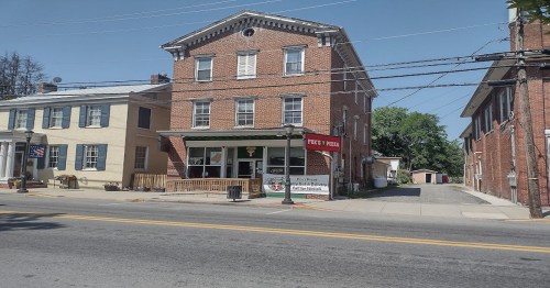 A brick building with a pizza shop sign, located on a quiet street with trees and other buildings nearby.