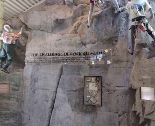 A rock climbing wall display with figures climbing and an informational sign about the challenge of rock climbing.