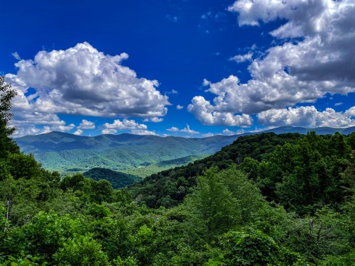A scenic view of lush green mountains under a bright blue sky with fluffy white clouds.