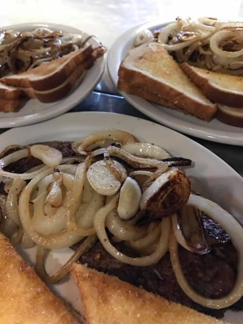 Plates of grilled meat topped with sautéed onions, served with toasted bread.