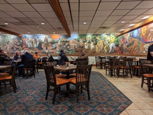 A vibrant restaurant interior with colorful murals, wooden tables, and patrons enjoying their meals.