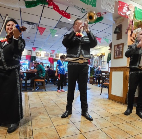 A mariachi band performs in a festive restaurant, with colorful decorations and diners enjoying the atmosphere.