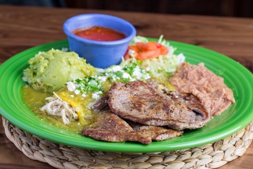 A vibrant plate of Mexican food featuring grilled meat, guacamole, refried beans, salad, and salsa in a blue bowl.