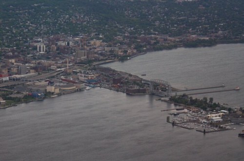 Aerial view of a city by the water, featuring buildings, a bridge, and a marina along the shoreline.