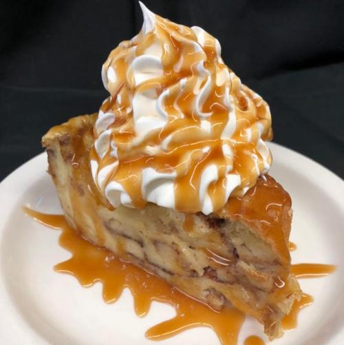 A slice of dessert topped with whipped cream and drizzled with caramel sauce on a paper plate.