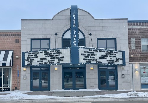 The River Cinema marquee displays movie titles, including "Ghostbusters" and "West Side Story," in a snowy setting.