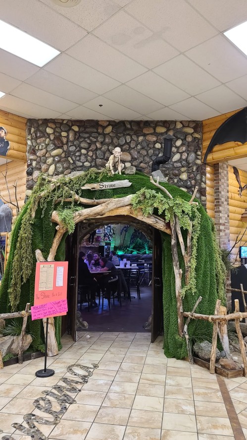 Entrance to a themed restaurant with a stone wall, greenery, and rustic decor, creating a cave-like atmosphere.