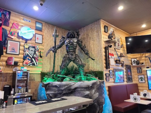 A detailed statue of a warrior stands on a rock in a themed restaurant, surrounded by colorful decor and artwork.