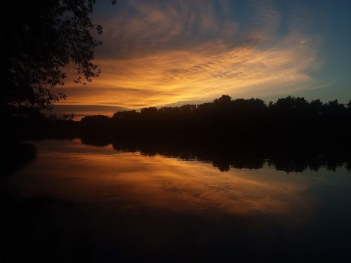 A serene sunset over a calm river, with vibrant orange and blue hues reflecting on the water's surface.