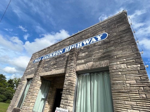 Exterior of a stone building with a sign reading "344 Jackson Highway" against a blue sky with clouds.