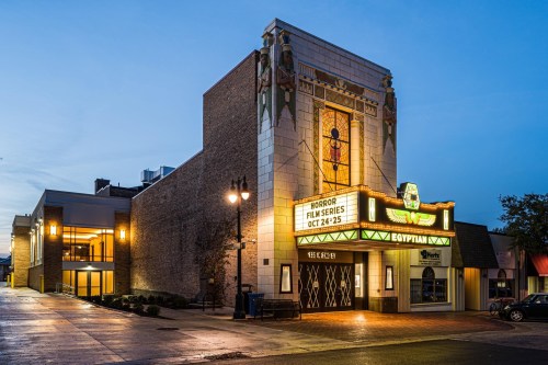 Historic theater building with a marquee advertising a horror film series, illuminated at dusk.