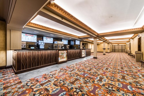 Interior of a theater lobby featuring a concession stand, decorative carpet, and illuminated ceiling.
