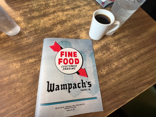 A menu from Wampach's restaurant in Saugatuck, MI, next to a cup of coffee on a wooden table.