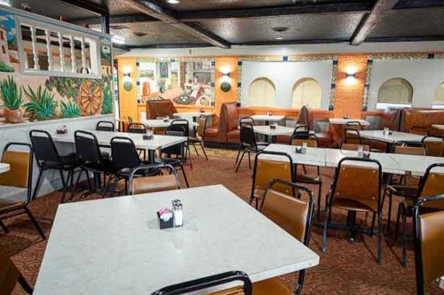 Interior of a restaurant featuring empty tables, chairs, and colorful wall decor with a cozy atmosphere.