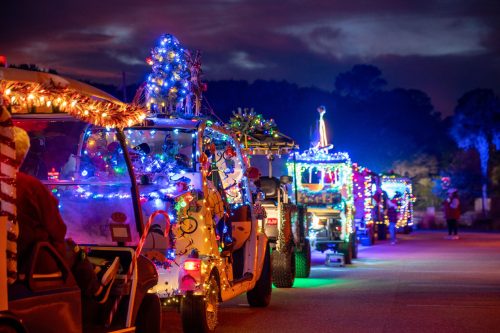 A line of decorated golf carts with colorful lights and festive ornaments, set against a night sky.