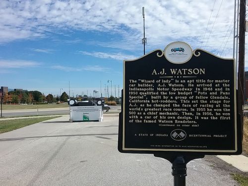 Sign about A.J. Watson, master car builder, at the Indianapolis Motor Speedway, with a view of the track in the background.