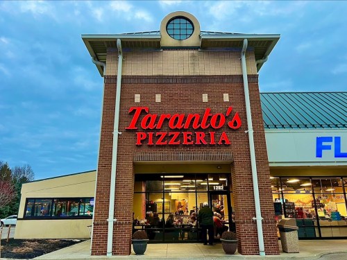 Exterior of Taranto's Pizzeria with a brick facade and large sign, under a cloudy sky.