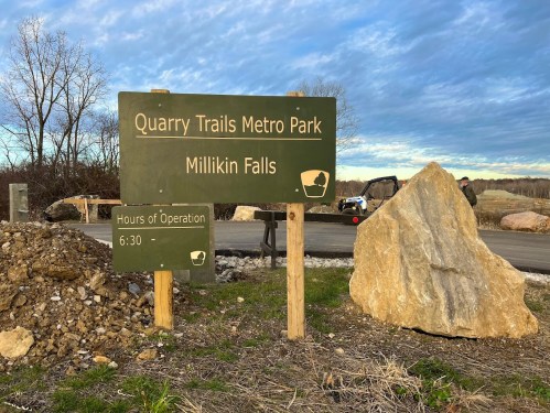 Sign for Quarry Trails Metro Park, Millikin Falls, with hours of operation listed, surrounded by natural scenery.