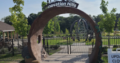 Archway entrance to Innovation Hills park, surrounded by greenery and a sign indicating updates and closures.