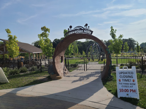 Entrance to Innovation Hills park with a sign indicating updated closing time at 10:00 PM. Lush greenery surrounds the area.
