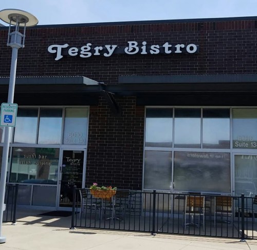 Exterior view of Tegry Bistro, featuring large windows and a sign, with outdoor seating visible.