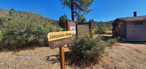 Sign for Johnston Ridge Trailhead with a building and trees in the background under a clear blue sky.