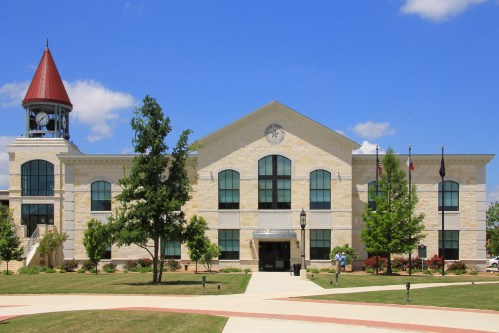 A modern stone building with a red roof, clock tower, and landscaped grounds under a blue sky.