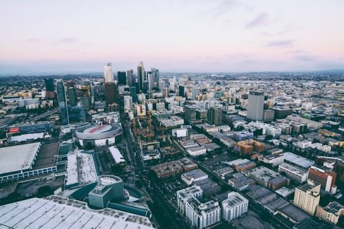 Aerial view of a city skyline at dusk, featuring tall buildings and urban streets.