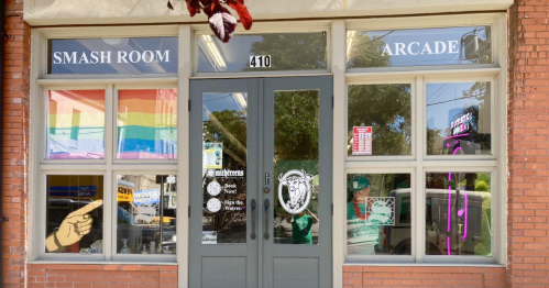 Exterior of a building with "Smash Room" and "Arcade" signs, featuring rainbow flags in the windows.