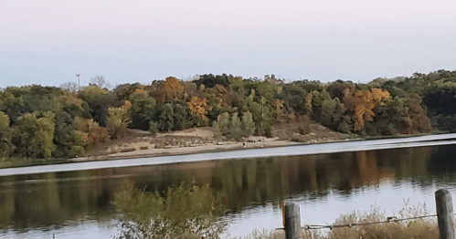A serene river scene with trees displaying autumn colors reflected in the calm water.