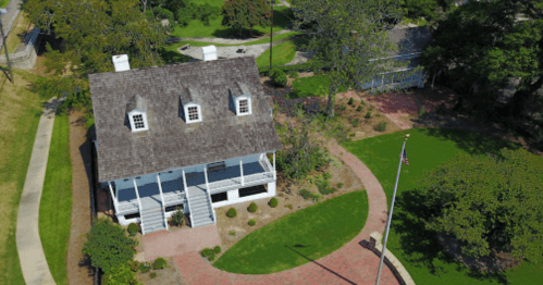 Aerial view of a historic house with a porch, surrounded by green lawns and pathways.