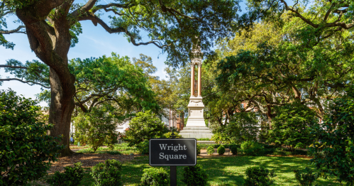 A monument in Wright Square surrounded by lush greenery and trees under a clear blue sky.